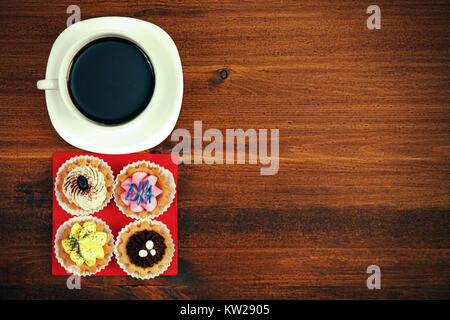 Tasse Tee oder Kaffee und vier Cupcakes auf braunen Tisch. Top Aussicht Stockfoto