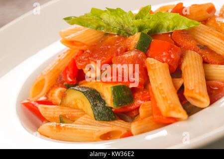 Nahaufnahme der Pasta mit Tomaten, Zucchini und Basilikum auf einem weißen Teller Stockfoto