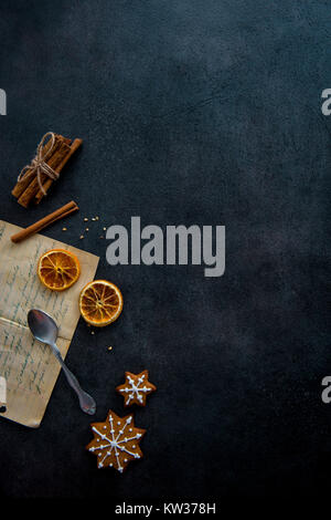 Zubereitung von Speisen. Altes Rezept und einige Zutaten (Zimtstangen, getrocknete Orangenscheiben) mit zwei sternförmigen Lebkuchen Kekse mit Zuckerguss. Stockfoto