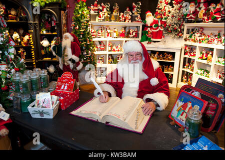 USA Virginia Williamsburg VA Santa Claus Weihnachtsmann Saint Nicolas in seinem Stuhl in seiner Werkstatt, die eine Liste in seinem Buch sitzen Stockfoto