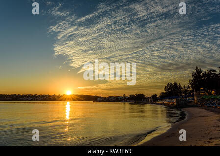 Sunrise mit vereinzelten weißen Wolken auf einem goldenen blauen Himmel über einen Strand und Meer Stockfoto