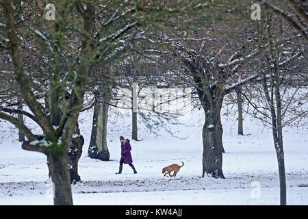 Eine Frau und ihr Hund zu Fuß durch eine verschneite Kelvingrove Park in Glasgow. Großbritannien sah einer der kältesten Nächte des Jahres mit Temperaturen von minus 12,3 C am Loch Glascarnoch in den schottischen Highlands. Stockfoto