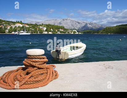 Ein kleines Schlauchboot mit Aussenbordmotor festgebunden an einem Kai durch ein Seil um einen Poller Stockfoto