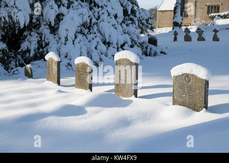 Schnee bedeckt Grabsteine in St. Bartholomä Kirchhof im Dezember Schnee. Notgrove, Cotswolds, Gloucestershire, England Stockfoto