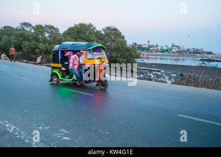 Eine überladene Auto-rikscha trägt seine Passagiere auf den Müll und Klärschlamm verseuchte Meer Strand in Madh Island, Indien. Stockfoto