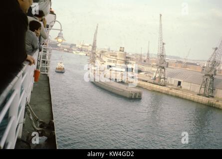 Passagiere Lean über die Schienen der Queen Elizabeth 2 Kreuzfahrtschiff der Cunard Line, da es Ansätze eines Ports, 1975. Stockfoto