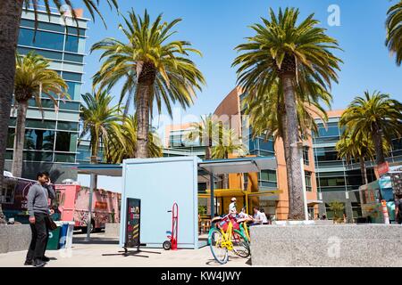 Im Googleplex, dem Sitz der Firma Google Search Engine im Silicon Valley Stadt Mountain View, Kalifornien, einem bunten Google Fahrrad ist in der Nähe von Essen LKW geparkt, mit Palmen und Gebäude der Google Campus im Hintergrund sichtbar, Mountain View, Kalifornien, 24. August 2016. Stockfoto