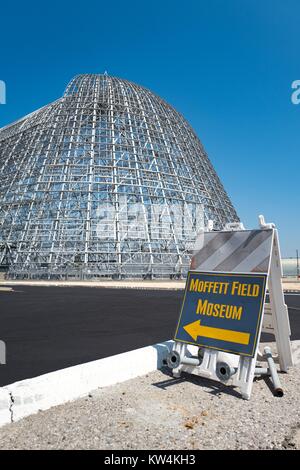 Schild mit Pfeil Besucher Regie der Moffett Field Historisches Museum, mit Hangar Eine im Hintergrund sichtbar, im sicheren Bereich des NASA Ames Research Center Campus im Silicon Valley Town in Palo Alto, Kalifornien, 25. August 2016. Hangar, die zu den weltweit größten freistehenden Strukturen, war zu Google Inc affiliate Planetarischen Ventures in 2016 (zusammen mit Moffett Field") für 60 Jahre zu einem Preis von $ 1,6 Mrd., bedingt durch die Unternehmen die Sanierung der Struktur, Kalifornien vermietet. Stockfoto