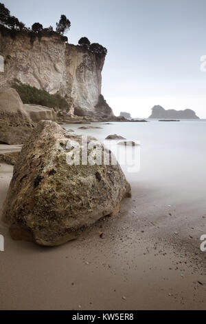 Unter den Klippen, Sand und Geröll zu einem atmosphärischen nebligen Tag auf der Coromandel, North Island, Neuseeland Stockfoto