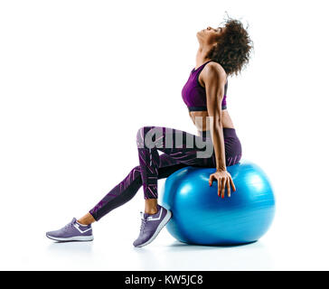 Mädchen ruht auf Gymnastikball. Foto von sportlichen afrikanisches Mädchen in Sportkleidung auf weißem Hintergrund. Sport Stockfoto