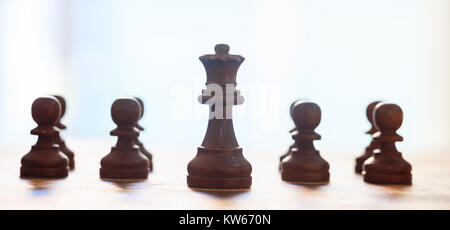 Schachfiguren dunkle braune Farbe. Nahaufnahme der Königin und Bauern mit Details. Unscharfer Hintergrund. Stockfoto