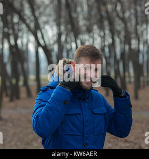 Portrait eines bärtigen Mannes im Winter Kleidung auf einem unscharfen Hintergrund der Bäume. Lächelnd bärtigen Geschäftsmann. Bärtiger Mann. Stockfoto