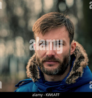Portrait eines bärtigen Mannes im Winter Kleidung auf einem unscharfen Hintergrund der Bäume. Lächelnd bärtigen Geschäftsmann. Panierte Menschen. Outdoor. Stockfoto