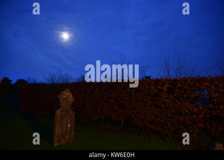 Vollmond durch die Wolken über einen Grabstein in der Kirche, Friedhof, Devon, England scheint. Stockfoto