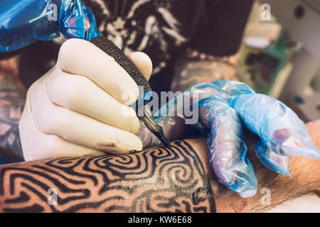 Nahaufnahme von einem professionellen Tätowierer mit Handschuhen Tätowieren ein Tribal Design auf dem linken Unterarm eines Kunden, Frankreich. Stockfoto