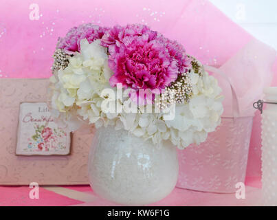 Blumenschmuck mit weißen Hortensie und rosa Pfingstrosen in einer weißen Vase gegen einen sanften Pastelltönen Hintergrund. Stockfoto