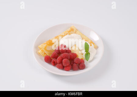 Platte von Crepes mit frischen Himbeeren und Sahne auf weißem Hintergrund Stockfoto