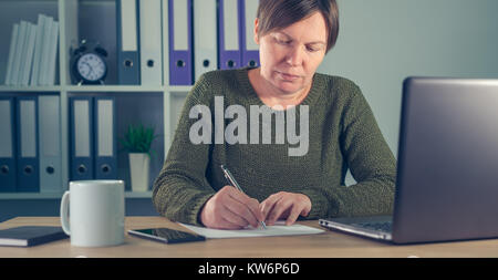 Geschäftsfrau Unterzeichnung Papiere oder das Schreiben von Notizen in Small Business Office Interior Stockfoto