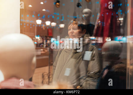 Nachdenkliche Frau durch Schaufenster in der Nacht suchen während der Weihnachten und Neujahr shopping rabatt Saison Stockfoto