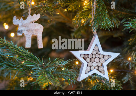 Holz- Stern- und Elche ornament hängend an einem Weihnachtsbaum mit Lichterketten Nahaufnahme Stockfoto