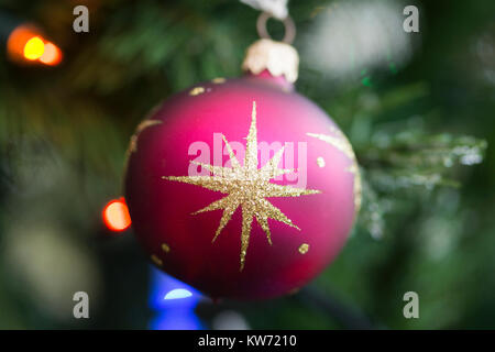 Eine Nahaufnahme einer einzelnen rosa Kugel Dekoration mit einem Gelber Stern, der an Weihnachten an einem Weihnachtsbaum hängt Stockfoto