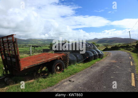 Alter Bauernhof Transport links am Straßenrand, um Rost, der sich mit tierischen Lebensmitteln in schwarz Ballen jenseits, der Halbinsel Dingle in der Grafschaft Kerry, Irland Stockfoto