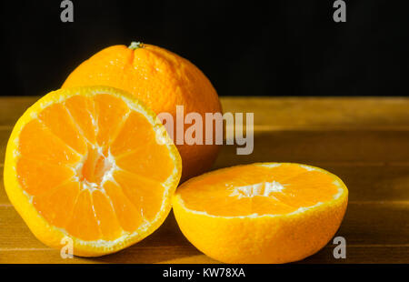 Reif Mandarin Obst geschält öffnen und auf alten rustikalen Look Holz mit Gruppe von Mandarin Früchte unscharf im Hintergrund Stockfoto