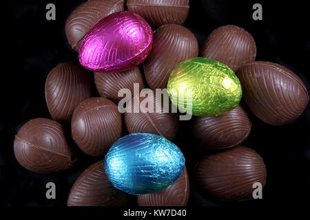 Stapel der Folie verpackt und unverpackt Schokolade Ostereier in rosa, blau und lime Green, vor einem schwarzen Hintergrund. Stockfoto