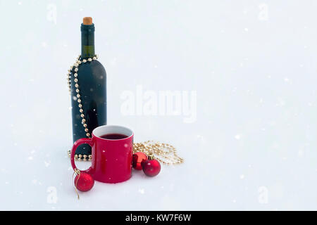 Flasche Wein mit roten Tasse und Weihnachtsschmuck auf Schnee mit Schnee vom Himmel Stockfoto