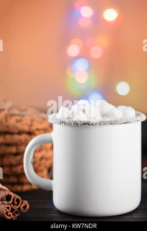 Emaille White Coffee Mug Tasse Kakao heißen Getränk trinken mit Marshmallow bei festlichen Hintergrund mit bokeh Girlande Dekoration Stockfoto