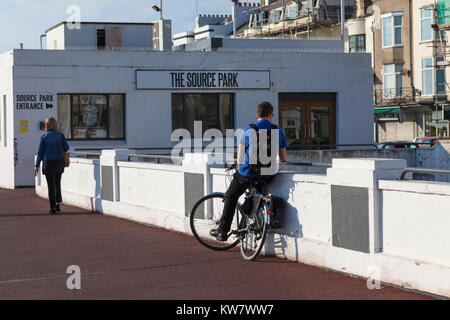 Ein junger Mann lehnt sich gegen eine Wand auf einem Fahrrad ausserhalb der Quelle Park, Hastings, East Sussex Stockfoto