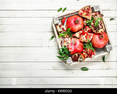 Reife Granatäpfel mit Blättern in das Feld ein. Auf einem weißen Holztisch. Stockfoto