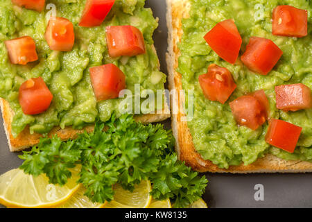 Nahaufnahme der Sandwiches mit lateinamerikanischen mexikanische Soße guacamole Avocado und weißes Brot Toast dekoriert gehackten Tomaten, in Scheiben geschnitten Zitrone auf Platte, ve Stockfoto