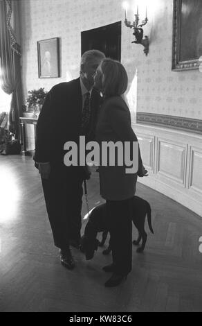 In einem Weißen Haus Esszimmer, Präsident Bill Clinton steht neben First Lady Hillary Rodham Clinton, beide trugen Pant Anzüge, lächelnd und flüstert in Ihr Ohr, halten eine Leine für erstes Haustier, Freund, dem Hund, für ein Mocha Brown Labrador, der zu ihren Füßen verfing sich ein Duft auf dem Fußboden, Washington, District of Columbia steht, 18. Dezember 1997. Stockfoto
