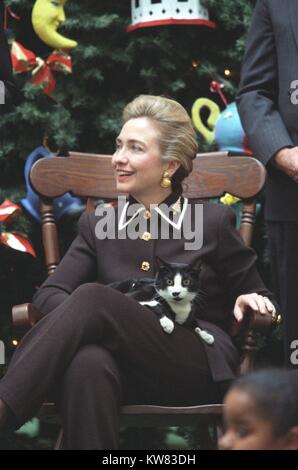 Socken die Katze, das erste pet von Präsident Bill Clinton und der First Lady Hillary Rodham Clinton, mit schwarzen Fell, weiße und gelbe Augen, sitzt auf dem Schoß der First Lady, das Tragen schwarzer Anzug mit goldenen Verzierungen, in einem hölzernen Stuhl vor einem großen, geschmückten Weihnachtsbaum sitzt, während der Ferien im Weißen Haus, Washington, District of Columbia, 13. Dezember 1995. Stockfoto