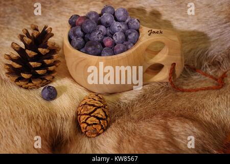 Heidelbeeren im Finnischen Holz- kuksy Schale auf ein Rentier Fell mit Kiefernzapfen. Nordeuropäischen noch Leben. Winter 2017. Stockfoto