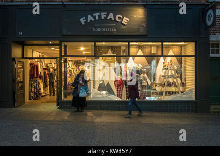 Zwei Frauen stand man einen Fuß außerhalb FatFace shop in Dorchester Dorset bei Dämmerung mit Orange glühen aus dem Store Front Stockfoto