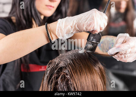 Attraktive Brünette gründlich färben Haare der weiblichen Klienten, während sie im Stuhl sitzt im Beauty Salon Friseur Stockfoto