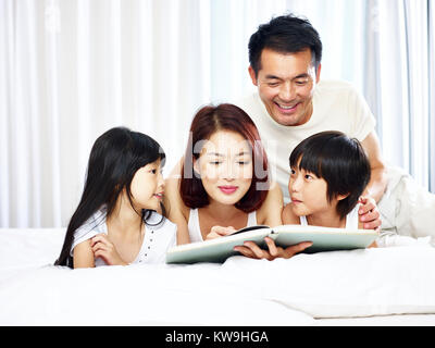 Asiatische Familie mit zwei Kindern mit einem Buch im Bett zu Hause. Stockfoto