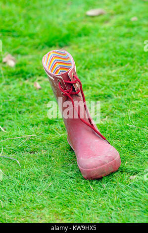 Asingled rot Wellington Boot von einem Kind in einem Feld von Gras verloren. Abgebrochene oder vergessen Bekleidung und Schuhe, Gummistiefel. Stockfoto