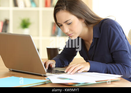 Konzentriert Unternehmer Vergleichen von Dokumenten auf Linie mit einem Laptop in einen Desktop zu Hause sitzen Stockfoto