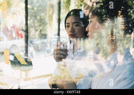 Asiatischer Mann & Frau diskutieren kreative Idee mit Haftnotizen auf Glas Wand am Arbeitsplatz. Haftnotiz Papier zur Erinnerung an office.Business, br Stockfoto