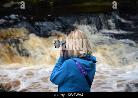 Eine Frau Fotograf Fotos von Stainforth Kraft Wasserfälle auf dem Fluss Ribble in Ribblesdale, Yorkshire Dales National Park, England, UK. Stockfoto