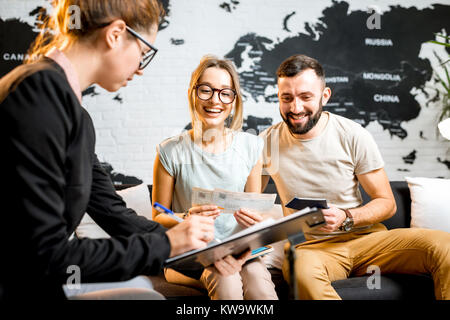 Junge paar schöne sitzend mit Manager im Reisebüro Büro prepairing für einen Sommerurlaub Stockfoto