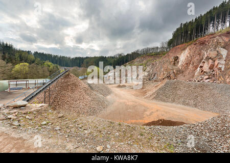 Ein großer Steinbruch in den Ardennen, Belgien mit dunklen Wolken, ein Rest von Wald auf dem Hügel. Stockfoto