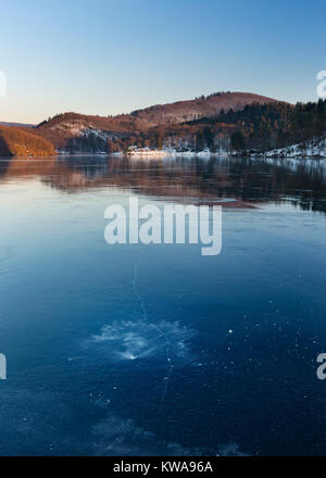 Abendlicher Blick über den zugefrorenen Obersee Rursee in der Nähe der Ortschaft Rurberg mit Schnee im Winter in der Eifel, Deutschland. Stockfoto