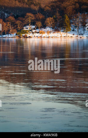 Abendlicher Blick über den zugefrorenen Obersee Rursee mit einem Haus, in der Nähe der Küste im Winter in der Eifel. Stockfoto