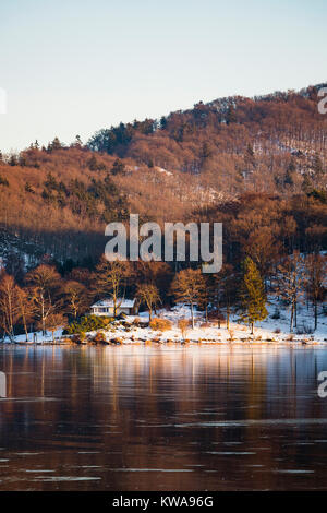 Abendlicher Blick über den zugefrorenen Obersee Rursee mit einem Haus, in der Nähe der Küste im Winter in der Eifel. Stockfoto