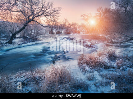 Winter Forest mit erstaunlichen Fluß bei Sonnenuntergang. Winterlandschaft mit verschneiten Bäumen, Eis, schöne zugefrorenen Fluss, verschneite Büsche, bunte Himmel in der Dämmerung. Blurre Stockfoto