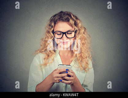 Junge Inhalt Frau in Brillen surfen Smartphone auf grauem Hintergrund. Stockfoto